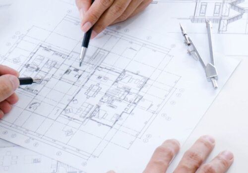 Image of floor plans being reviewed by an interior designer and an architect working together shown by both of their hands drawing on the plans